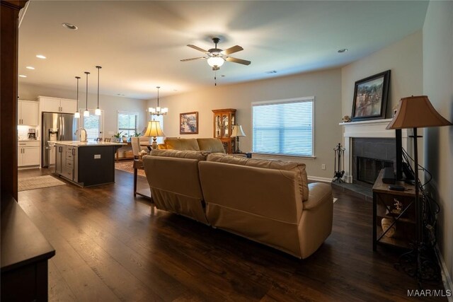 living room with ceiling fan with notable chandelier, dark hardwood / wood-style flooring, and a tiled fireplace