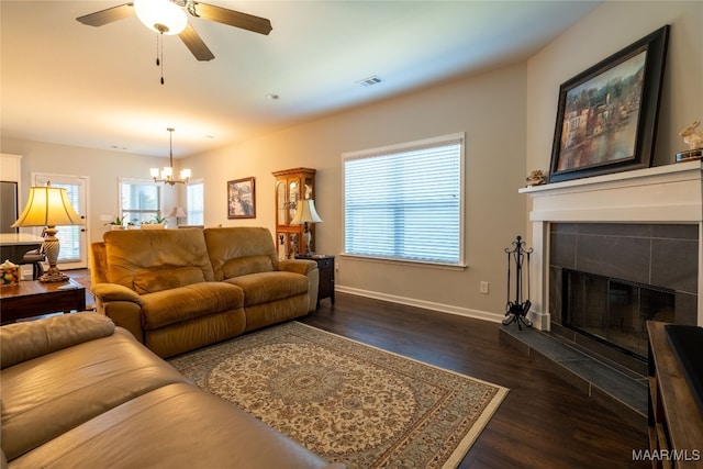 living room with ceiling fan with notable chandelier, dark hardwood / wood-style flooring, plenty of natural light, and a tiled fireplace