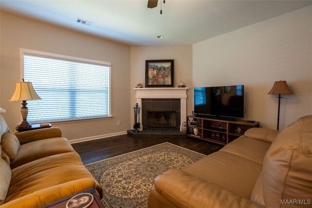 living room featuring ceiling fan, dark wood-type flooring, and a tiled fireplace