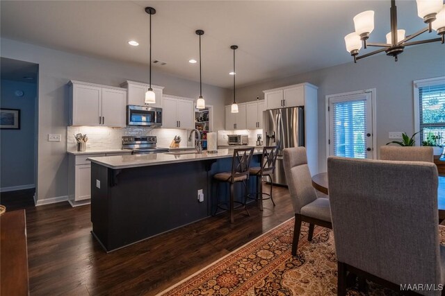 kitchen featuring appliances with stainless steel finishes, a kitchen island with sink, pendant lighting, white cabinets, and a chandelier