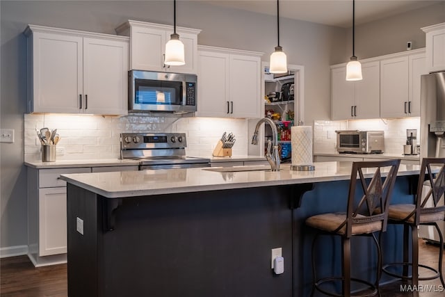 kitchen featuring a center island with sink, pendant lighting, white cabinetry, and stainless steel appliances