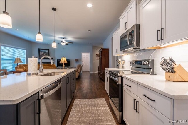 kitchen with decorative backsplash, appliances with stainless steel finishes, ceiling fan, a center island with sink, and hanging light fixtures