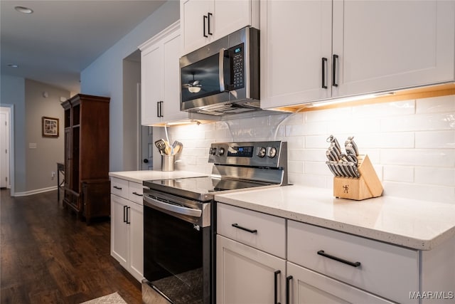 kitchen with dark wood-type flooring, stainless steel appliances, tasteful backsplash, light stone counters, and white cabinets