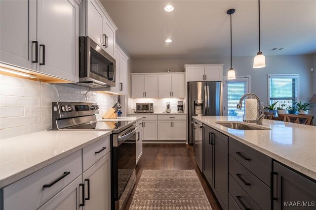 kitchen featuring light stone countertops, appliances with stainless steel finishes, sink, pendant lighting, and white cabinets