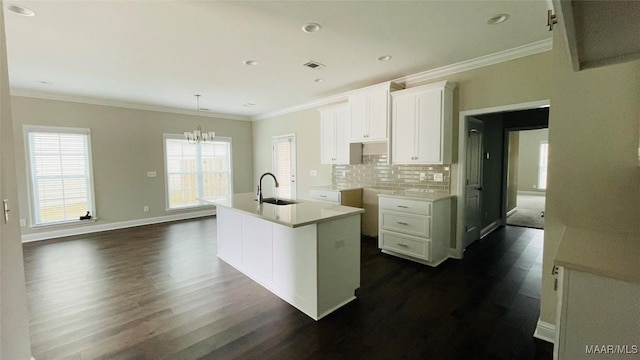 kitchen with sink, white cabinetry, backsplash, ornamental molding, and an island with sink