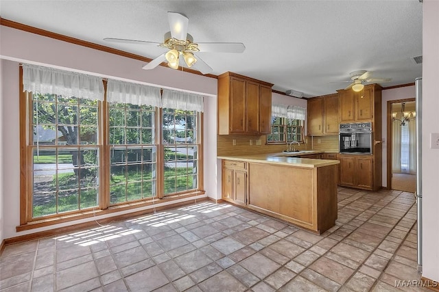 kitchen with crown molding, ceiling fan with notable chandelier, kitchen peninsula, decorative backsplash, and oven