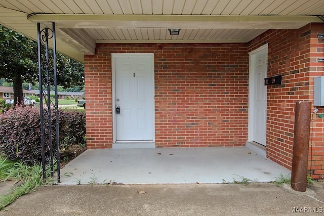 view of exterior entry featuring covered porch and brick siding