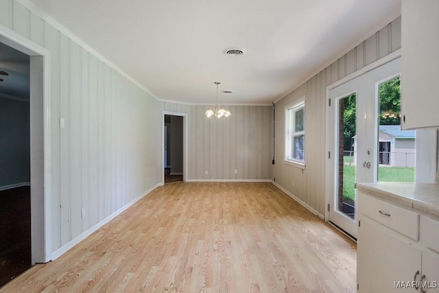 interior space with light wood-style flooring, a notable chandelier, visible vents, baseboards, and crown molding