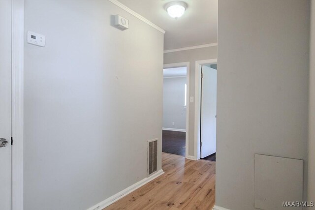 hall featuring light wood finished floors, baseboards, visible vents, and ornamental molding