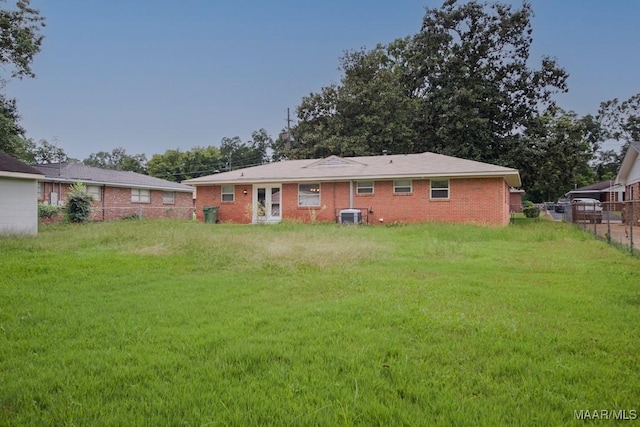 back of property with brick siding, a lawn, central AC unit, and fence