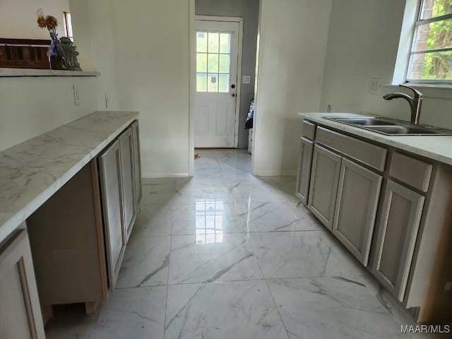 kitchen featuring marble finish floor, a sink, light stone countertops, and baseboards