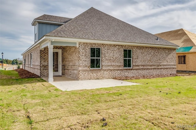 back of house with brick siding, roof with shingles, a yard, and a patio