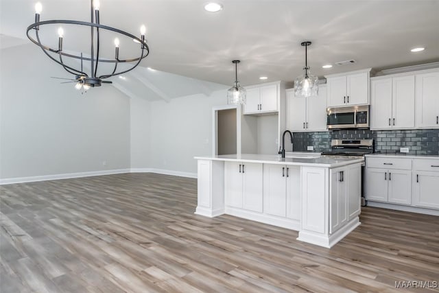 kitchen featuring stainless steel appliances, light countertops, hanging light fixtures, a kitchen island with sink, and white cabinetry