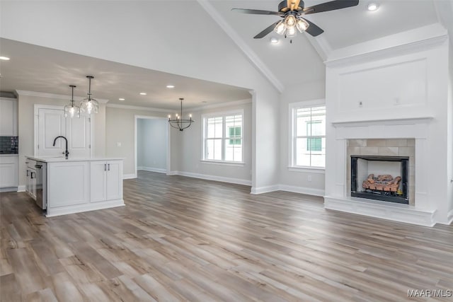 unfurnished living room with light wood-style floors, a fireplace with raised hearth, crown molding, and ceiling fan with notable chandelier