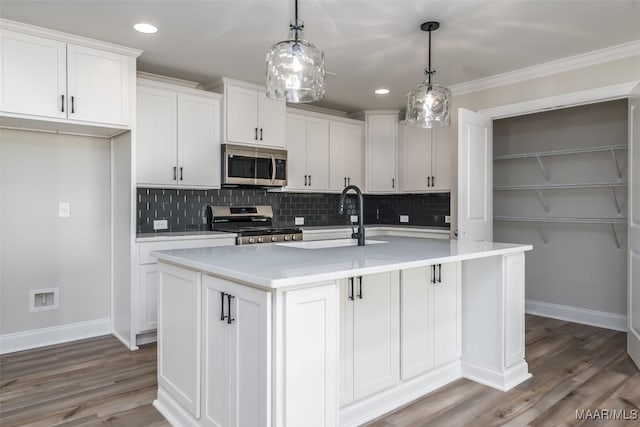 kitchen with a center island with sink, white cabinets, stainless steel appliances, light countertops, and pendant lighting