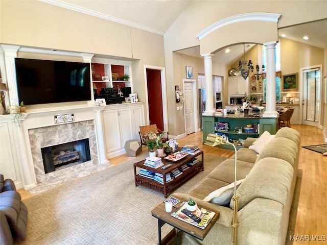 living room with decorative columns, a fireplace, high vaulted ceiling, and light hardwood / wood-style floors