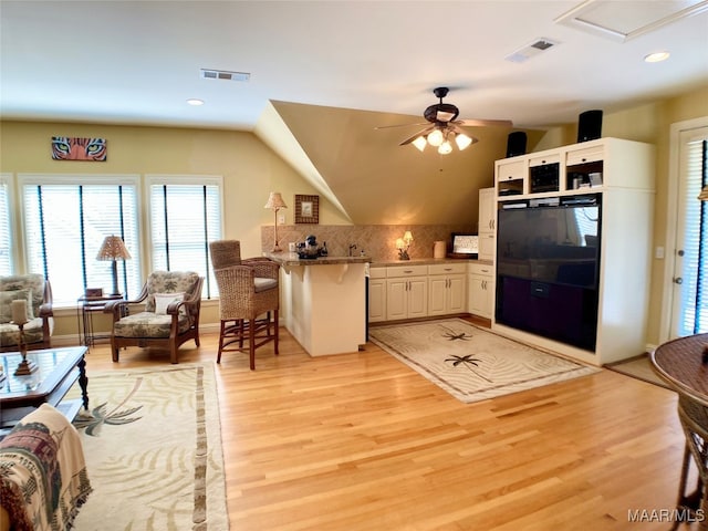 kitchen with decorative backsplash, a breakfast bar, ceiling fan, white cabinetry, and light hardwood / wood-style floors