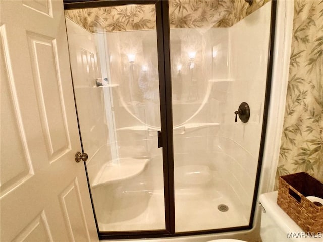bathroom with wallpapered walls, toilet, and a shower stall