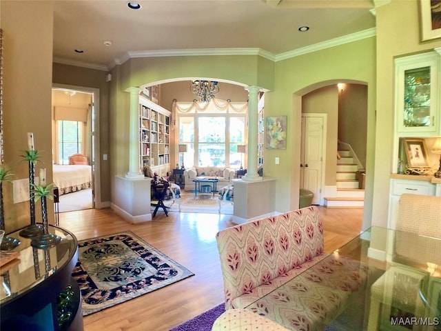 living area with crown molding, decorative columns, baseboards, arched walkways, and wood finished floors