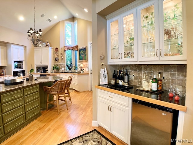 kitchen with lofted ceiling, appliances with stainless steel finishes, white cabinets, pendant lighting, and light hardwood / wood-style floors