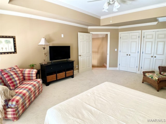 bedroom with two closets, ceiling fan, a raised ceiling, crown molding, and carpet flooring