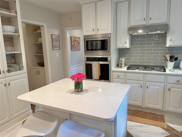 kitchen with tasteful backsplash, stainless steel appliances, light hardwood / wood-style floors, white cabinetry, and a center island