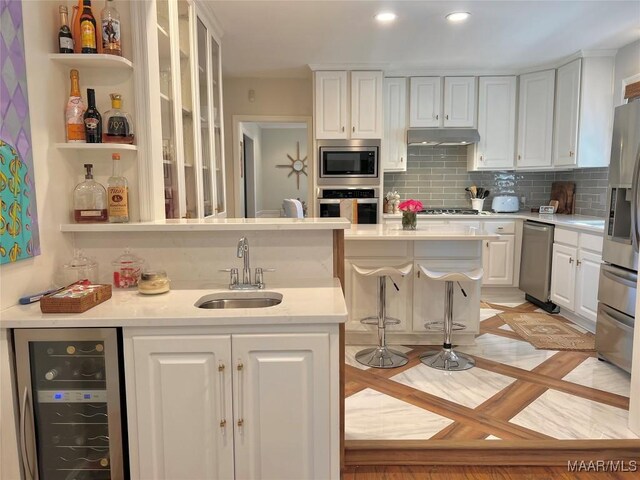 kitchen with stainless steel appliances, decorative backsplash, wine cooler, sink, and white cabinetry