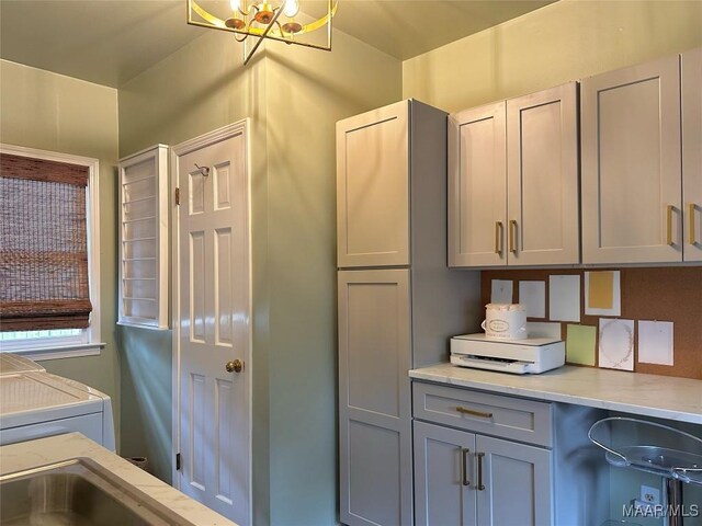 kitchen featuring light stone counters, gray cabinets, and a chandelier