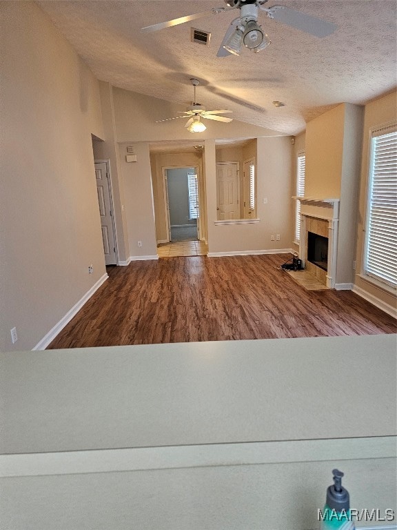 unfurnished living room featuring a textured ceiling, ceiling fan, vaulted ceiling, a tiled fireplace, and wood-type flooring