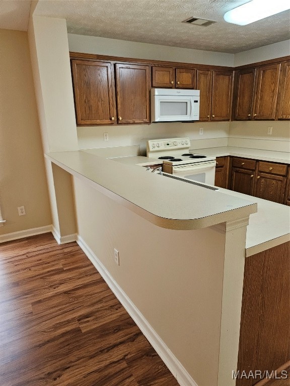 kitchen with white appliances, dark wood-type flooring, kitchen peninsula, and a textured ceiling