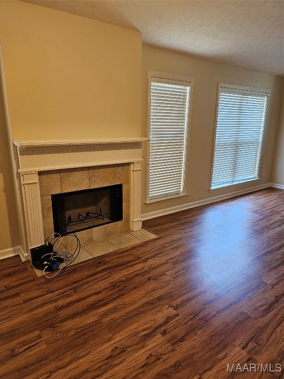 unfurnished living room featuring a tiled fireplace, a textured ceiling, and hardwood / wood-style flooring