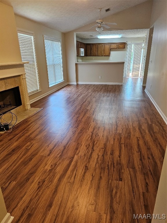 unfurnished living room featuring a textured ceiling, a tile fireplace, lofted ceiling, ceiling fan, and dark wood-type flooring