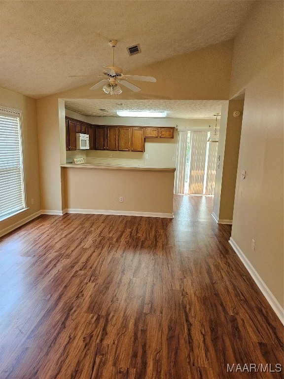 unfurnished living room with ceiling fan, dark wood-type flooring, lofted ceiling, and a wealth of natural light