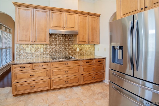 kitchen with light stone countertops, backsplash, stainless steel fridge, and black electric stovetop