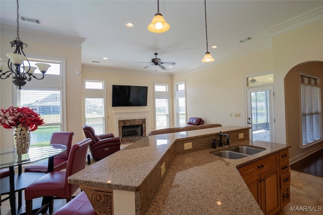 kitchen featuring light stone counters, sink, ornamental molding, pendant lighting, and a fireplace