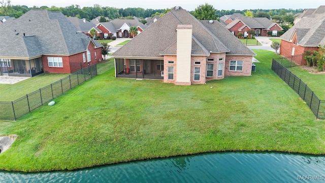 back of property featuring a sunroom, a yard, and a water view