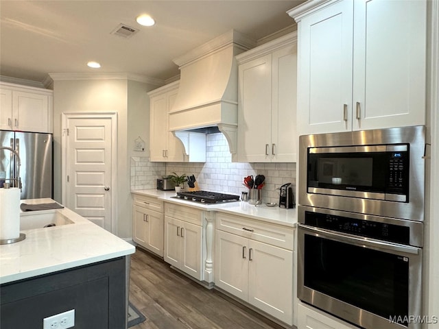 kitchen with appliances with stainless steel finishes, premium range hood, decorative backsplash, white cabinetry, and dark hardwood / wood-style flooring