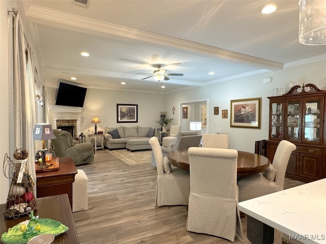 dining area with hardwood / wood-style floors, crown molding, ceiling fan, and a brick fireplace