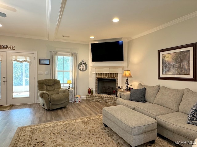 living room featuring beam ceiling, a brick fireplace, crown molding, and hardwood / wood-style floors