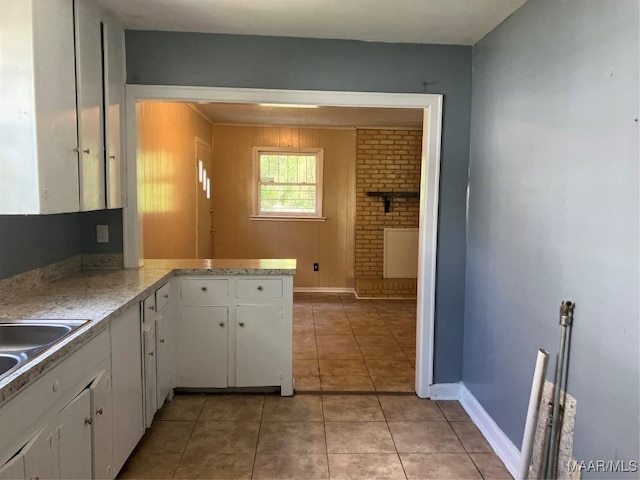 kitchen with light tile patterned flooring, kitchen peninsula, sink, and white cabinets