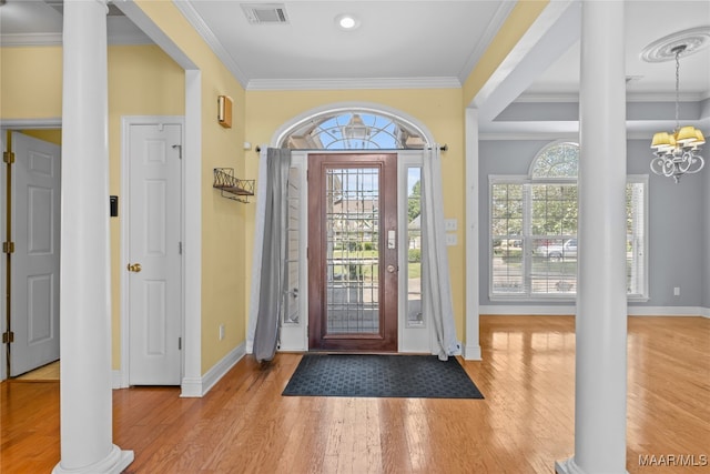 entrance foyer with ornate columns, ornamental molding, wood-type flooring, a chandelier, and a raised ceiling