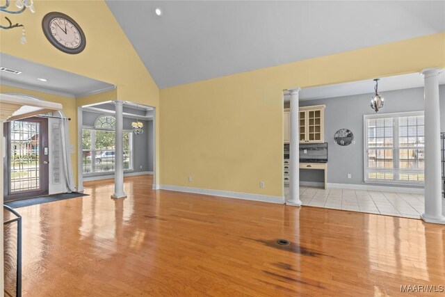 unfurnished living room featuring ornate columns, high vaulted ceiling, light hardwood / wood-style flooring, and a chandelier