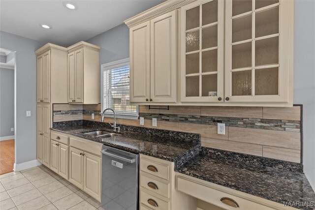 kitchen featuring dark stone counters, dishwasher, cream cabinets, light tile patterned floors, and sink