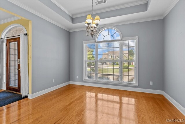 unfurnished room featuring a tray ceiling, crown molding, hardwood / wood-style floors, and a chandelier