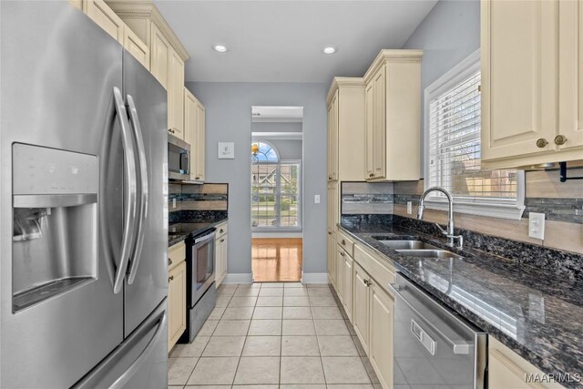 kitchen with appliances with stainless steel finishes, light tile patterned floors, sink, and dark stone counters