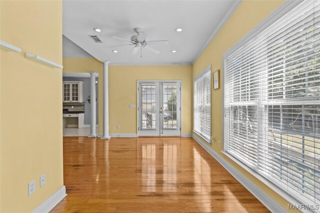 spare room featuring ornate columns, ornamental molding, french doors, light hardwood / wood-style floors, and ceiling fan