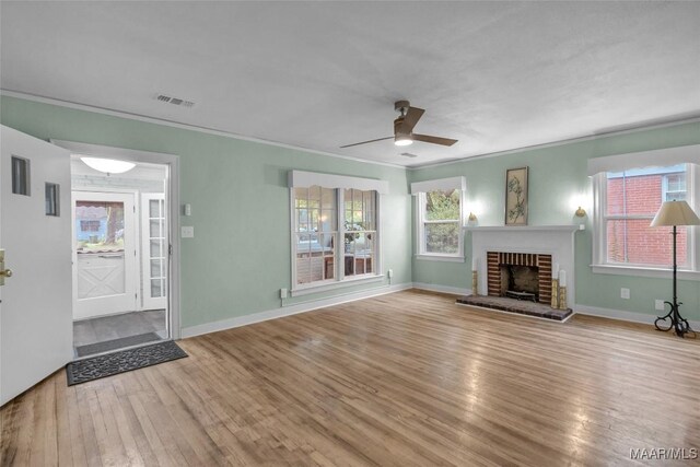 unfurnished living room with light wood-type flooring, crown molding, ceiling fan, and a brick fireplace