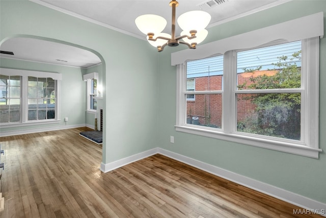 empty room with a notable chandelier, ornamental molding, and hardwood / wood-style flooring