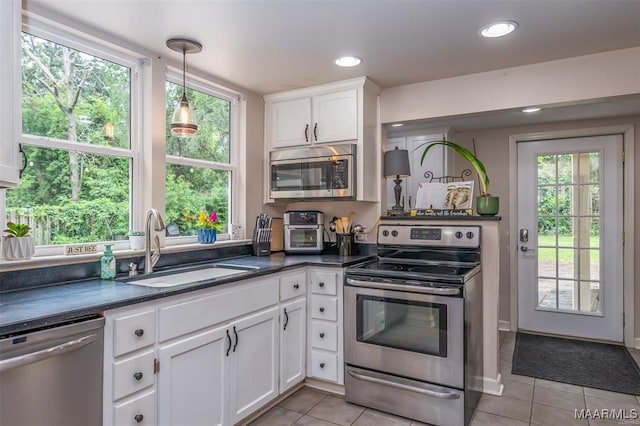 kitchen with light tile patterned flooring, sink, stainless steel appliances, pendant lighting, and white cabinets