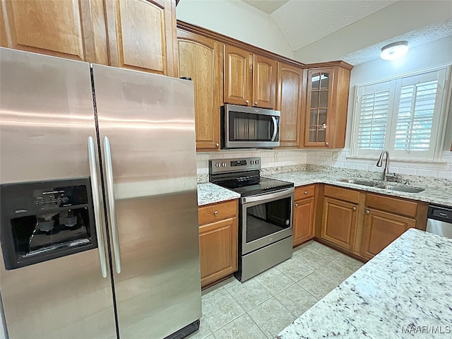 kitchen with sink, light stone countertops, stainless steel appliances, and vaulted ceiling